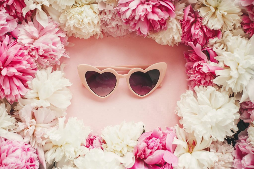 Pink heartshaped sunglassess in stylish pink and white peonies frame on pink paper